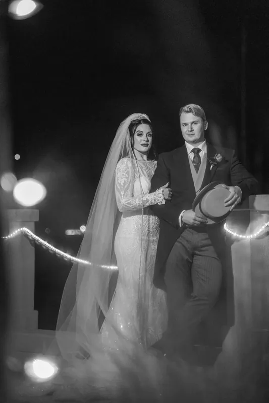 The couple walks hand-in-hand past glowing string lights after their evening ceremony.