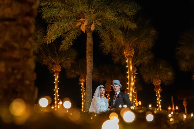 Illuminated palms frame Alyson and Sam standing together amid golden lights at The Treasury on the Plaza.