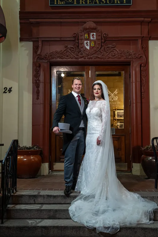 Alyson's lace gown flows down the historic entrance steps as Sam stands beside her in a dark suit.