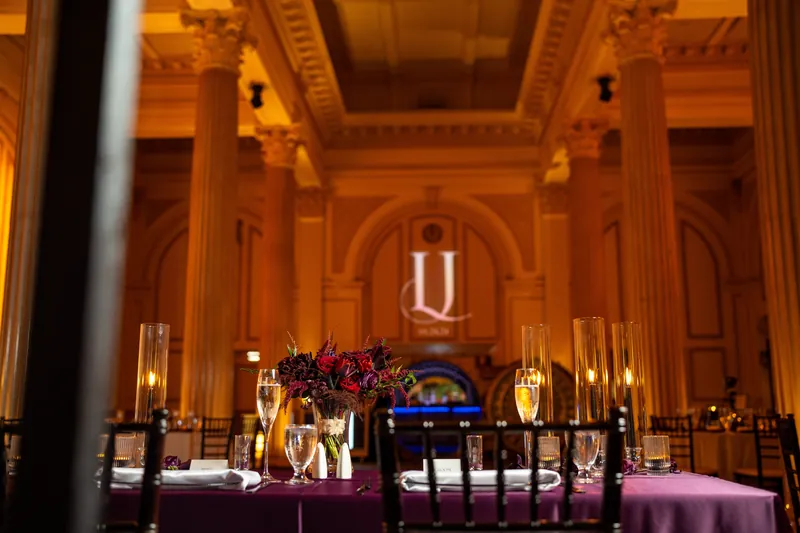 Crimson flowers and candlelit tables frame the altar in The Treasury's warm, gilded ceremony hall.