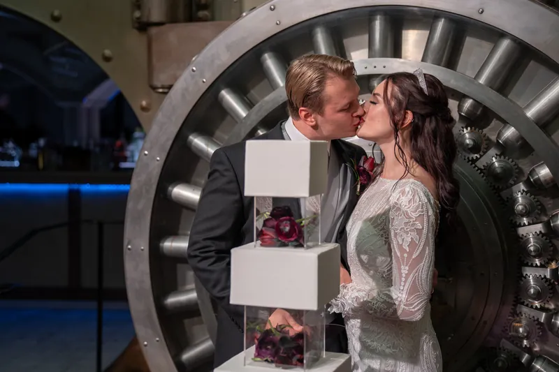Sam kisses Alyson near a large illuminated gear installation at their reception venue.