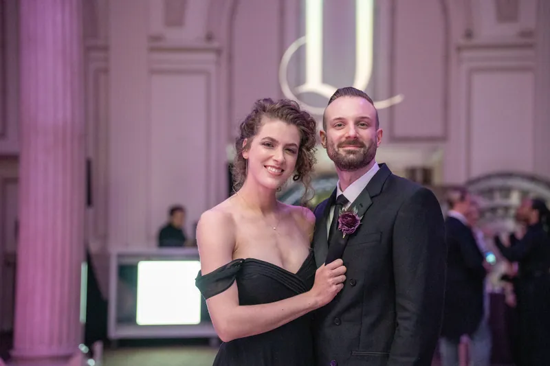 Two guests pose together at The Treasury on the Plaza in formal attire under purple lighting.