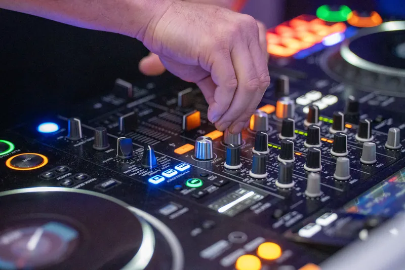 A DJ's hand adjusts colorful buttons and sliders on a mixer during the reception's music and dancing.