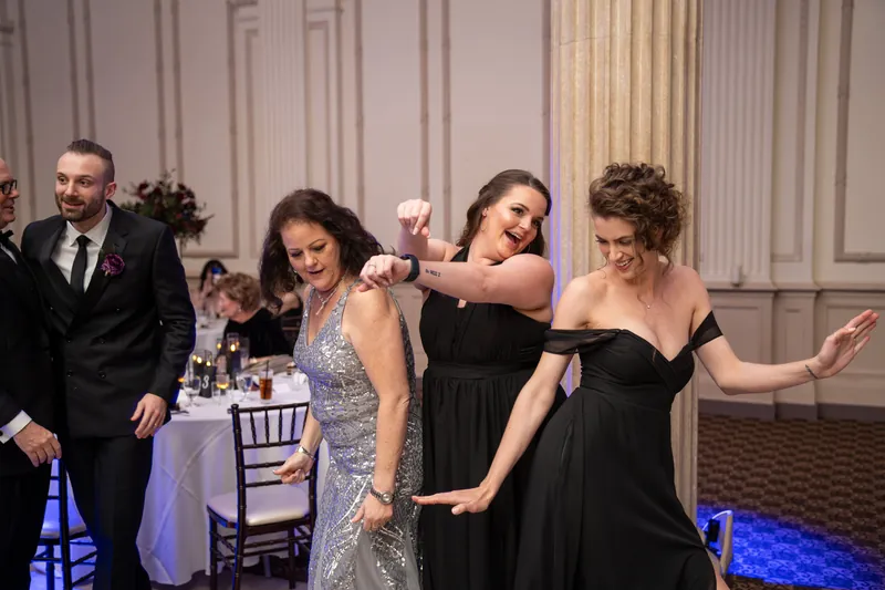 Four guests dance together in formal attire under blue accent lighting at The Treasury on the Plaza.
