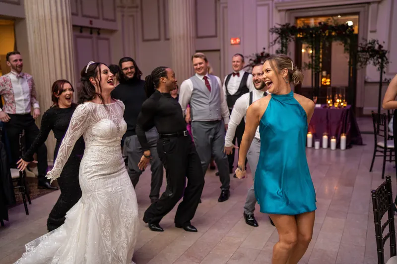 A guest in a white gown dances while another in bright blue joins the celebration.