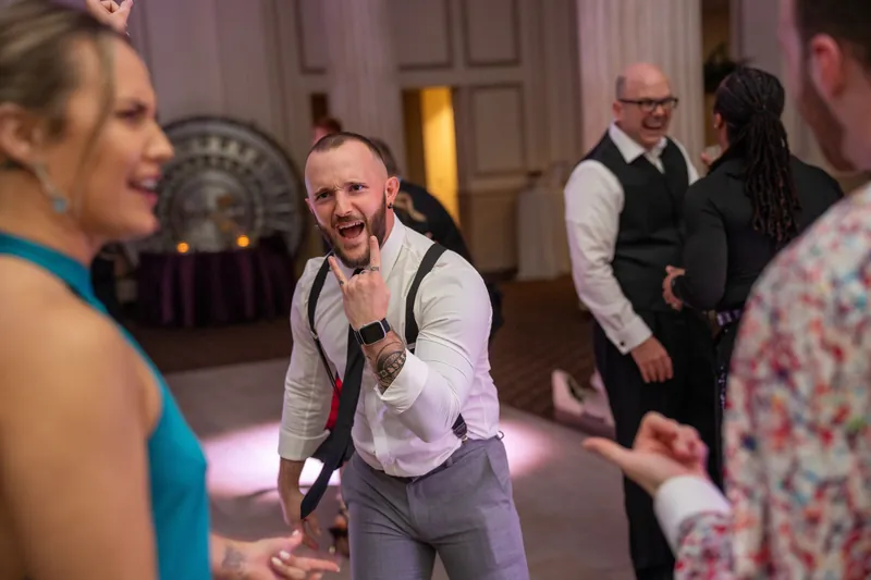 Sam grins mid-dance surrounded by guests as the evening celebration unfolds in the elegant historic venue.