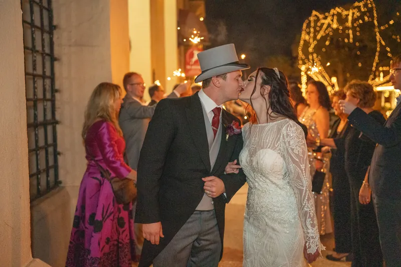 Sam leans in to kiss Alyson during their recessional, both wearing formal attire with golden wreaths glowing behind them.