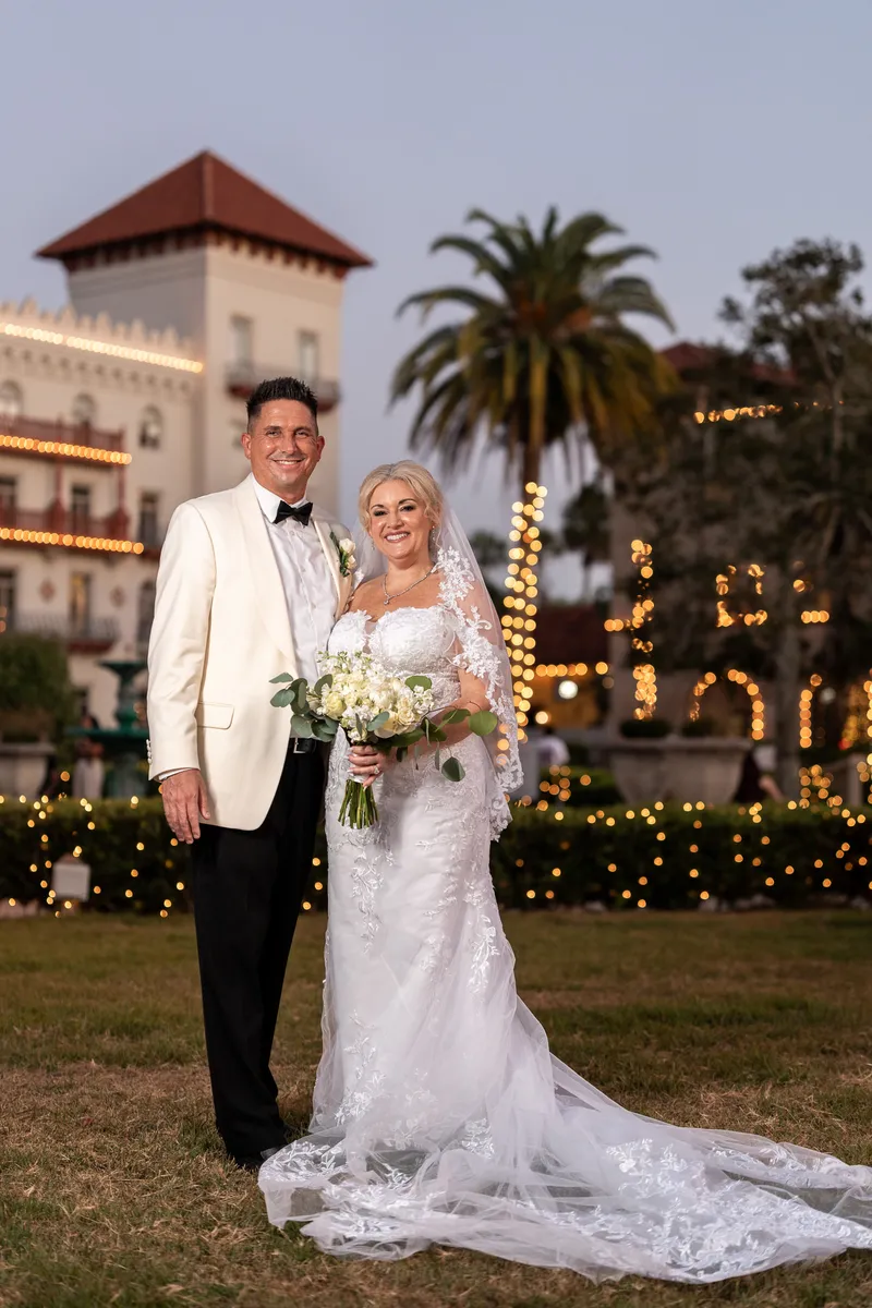 Amanda holds a white bouquet while Max smiles beside her under a massive oak tree at the St. Francis Inn.