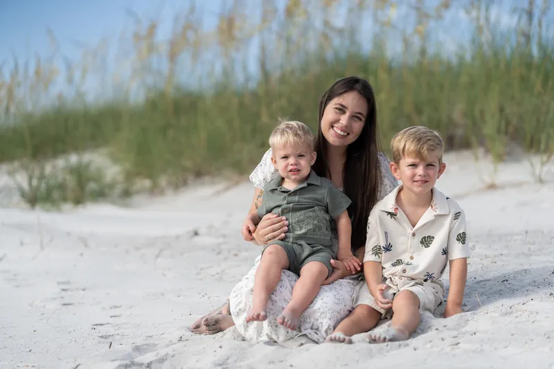Ana holds a toddler while sitting on the sand with an older boy beside them at Vilano Beach.