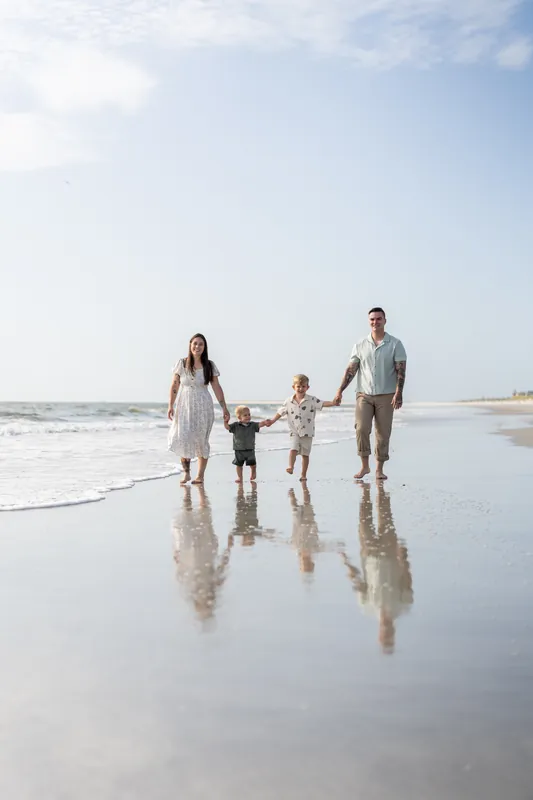 Ana and Bailey walk along the wet sand at Vilano Beach with their two children, their reflections visible in the shallow