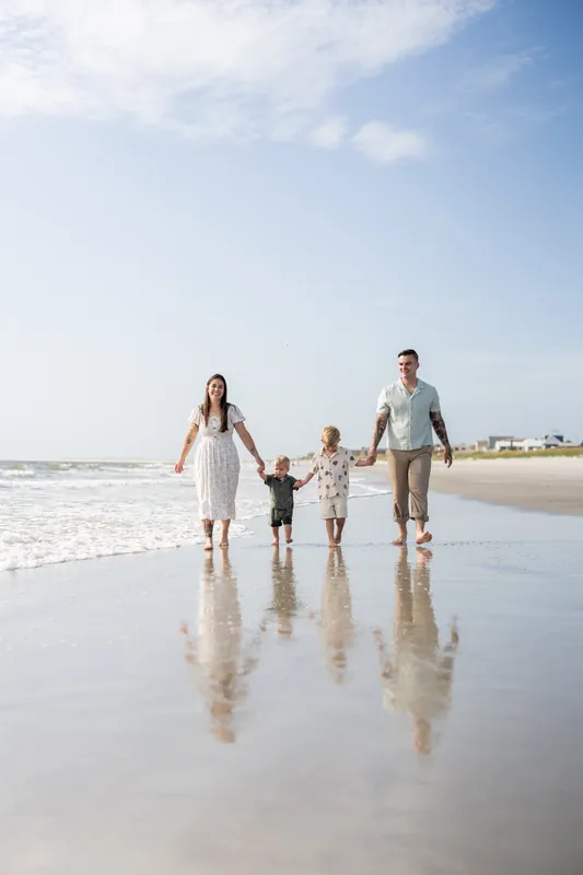 Ana, Bailey, and their two children walk hand-in-hand through shallow waves at Vilano Beach, St. Augustine, under clear