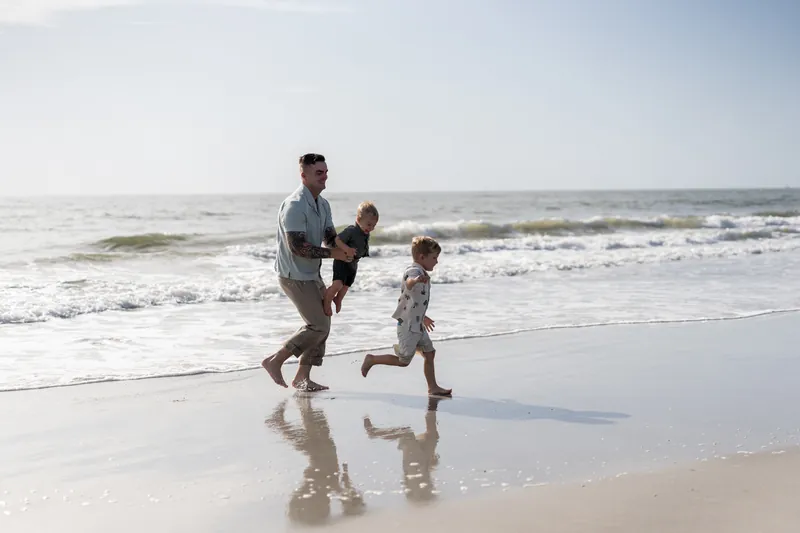 Bailey runs with their two children along the wet sand at Vilano Beach, St. Augustine, as waves roll in behind them.