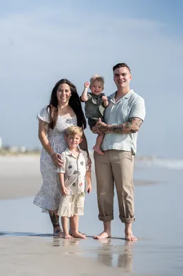 The family poses together on a shaded path lined with trees, with Bailey holding one child while Ana stands beside them.
