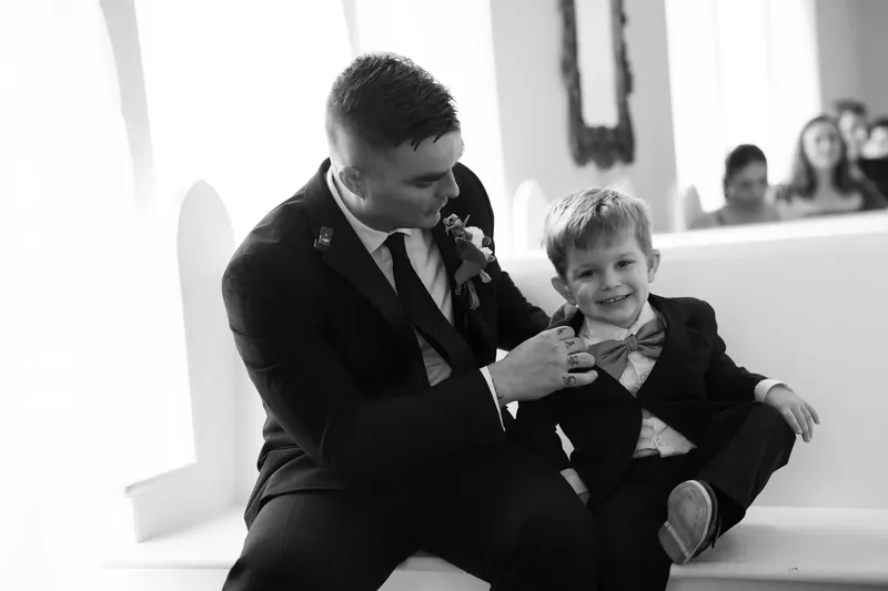 A man in a black suit and young child in formal wear share a moment together.