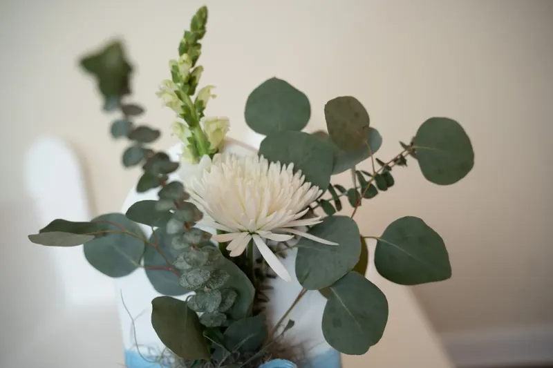 A bridal bouquet features white chrysanthemums, eucalyptus, and trailing greenery.