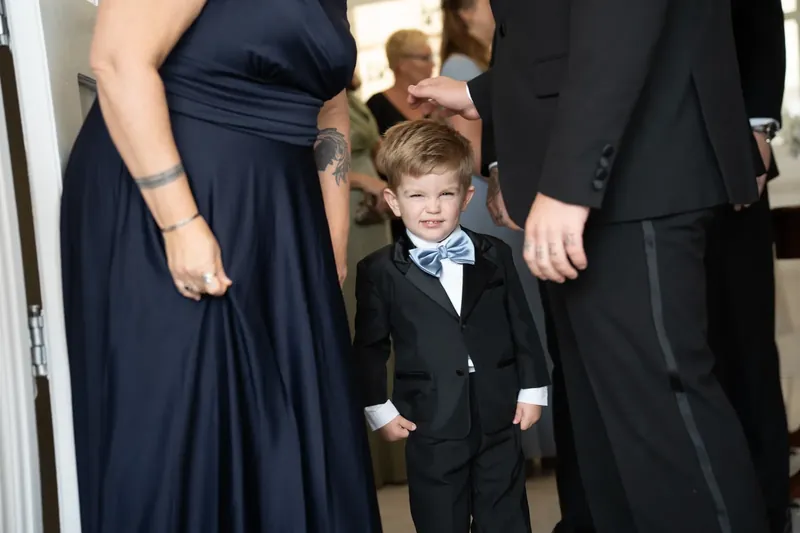 A small child in a black suit stands between two adults in formal attire inside the chapel during the ceremony.