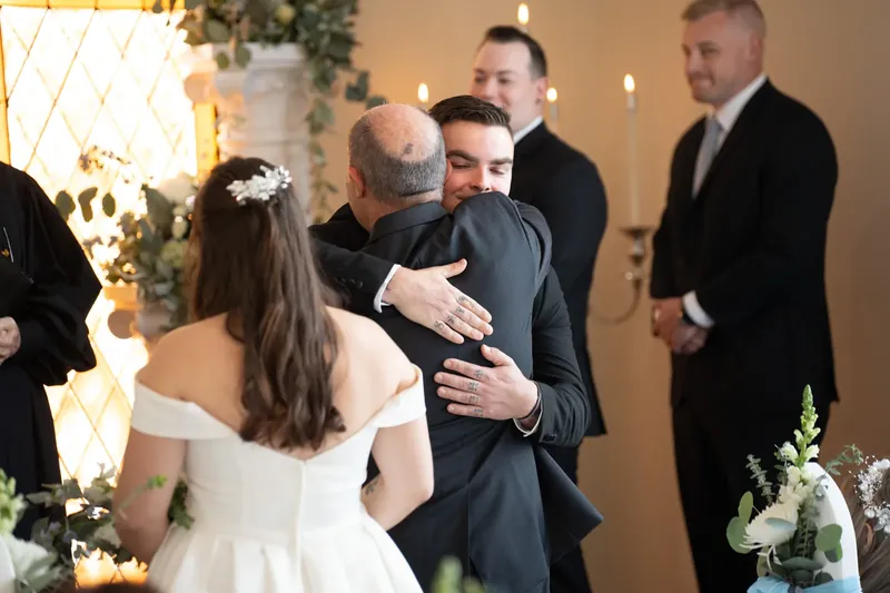 Ana and Bailey embrace during their ceremony at Amore Wedding Chapel, surrounded by family and attendants in formal attire.