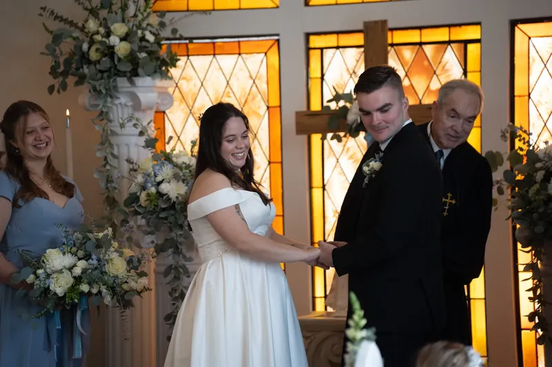 Ana in a white off-shoulder gown exchanges rings with Bailey as a clergy member presides over the ceremony.
