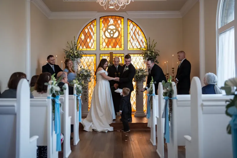 Ana and Bailey stand together at the altar with guests seated in white pews on either side of the chapel.