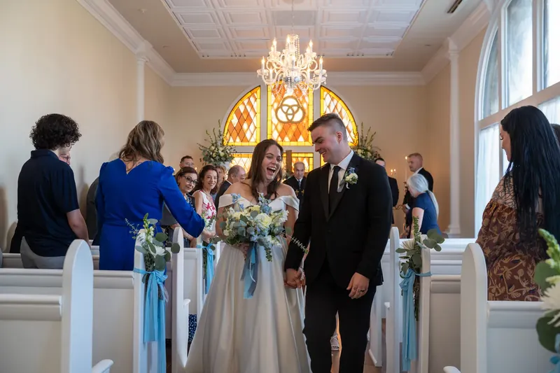 Ana and Bailey walk back down the aisle together as newlyweds, beaming with guests rising to celebrate them.