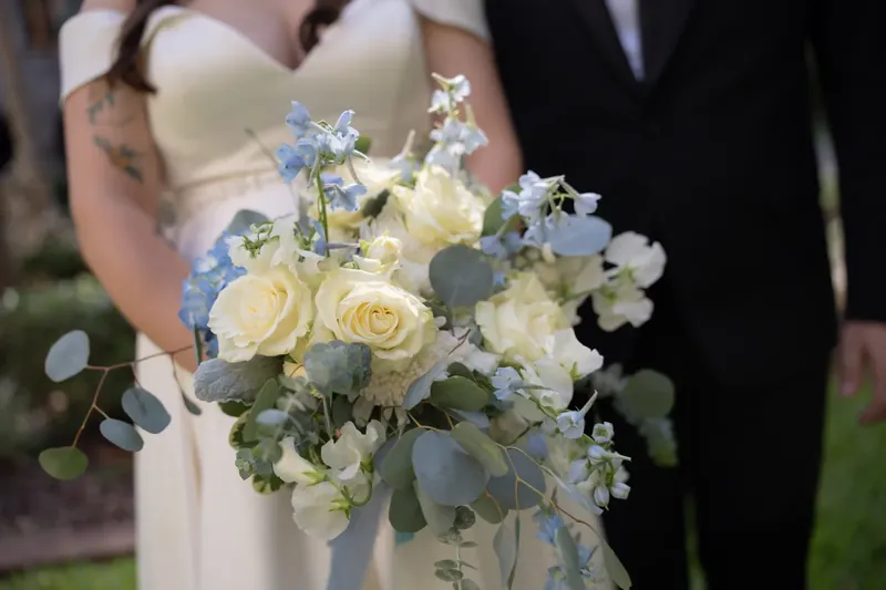 Close-up of Ana's bouquet featuring cream roses, white flowers, and blue accents against her white gown.