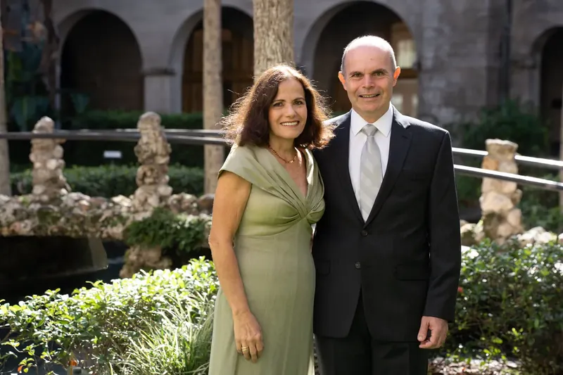 A woman in a sage green dress and a man in a dark suit smile together in the museum's courtyard.