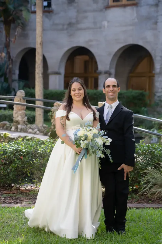 Bailey holds a white and green bouquet while standing with Ana on the grass at the Lightner Museum.
