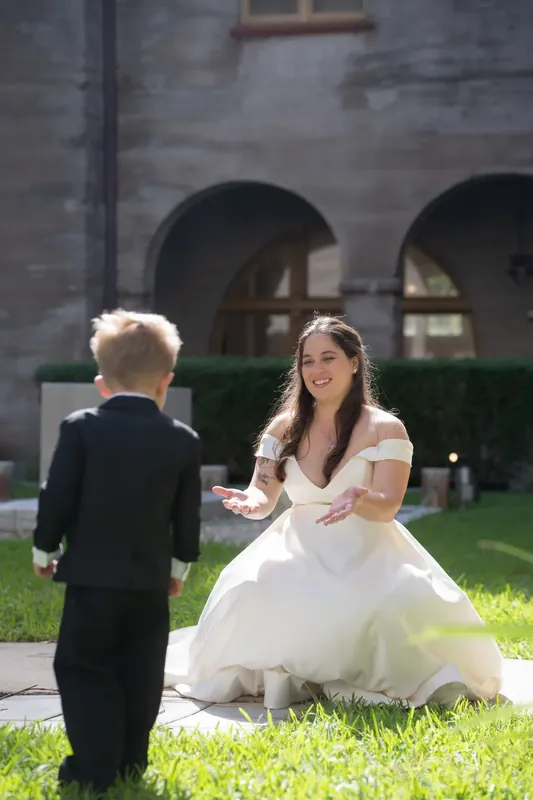 Ana kneels on the lawn to speak with a small child in formal wear as the museum's architecture rises behind them.