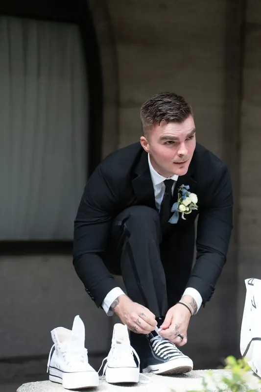 Bailey sits tying white sneakers, a boutonniere pinned to his dark suit jacket.
