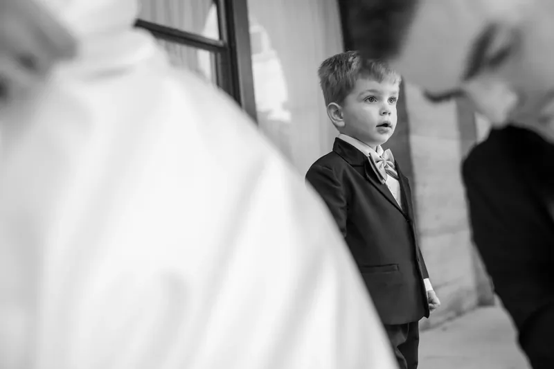A young ring bearer in formal attire stands quietly near flowing white fabric during the ceremony.