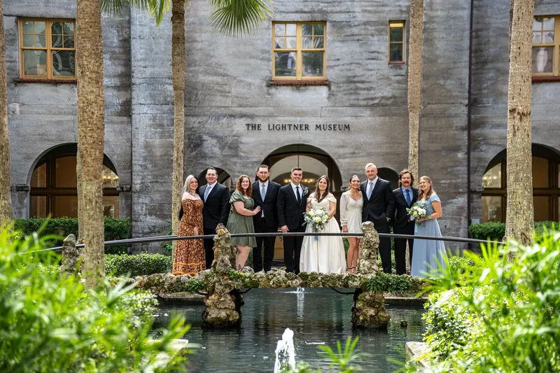 Ana and Bailey stand with their wedding party on a colonnade overlooking the courtyard pool at Lightner Museum.