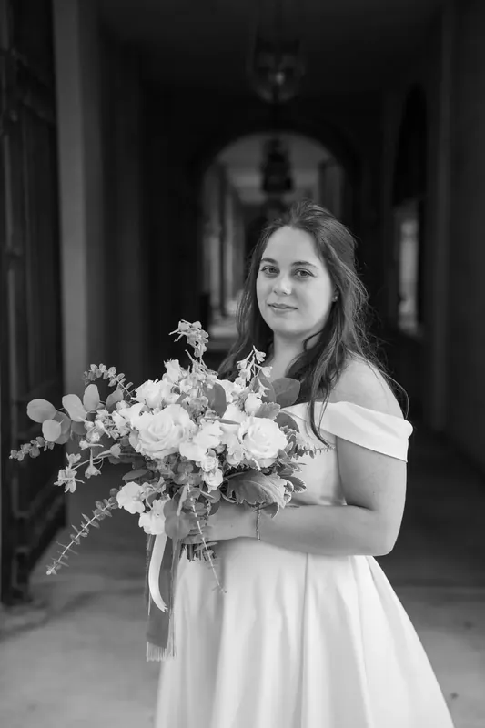 Ana holds her white and green bouquet while gazing over her shoulder at Lightner Museum.