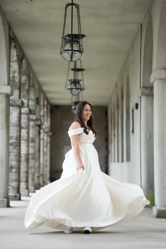 Bailey twirls in her flowing white dress beneath the arched colonnade at Lightner Museum, fabric sweeping around her.