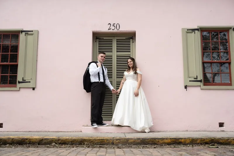 Ana and Bailey stand at the pink Lightner Museum facade, she in white and he in a dark suit with suspenders.