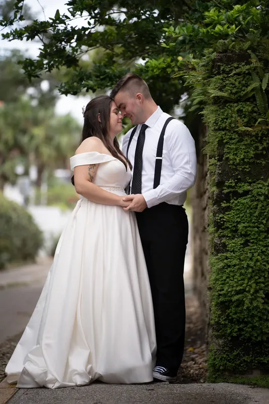 The couple kiss along a lush ivy-lined pathway, with Ana's off-shoulder gown flowing as Bailey holds her close.