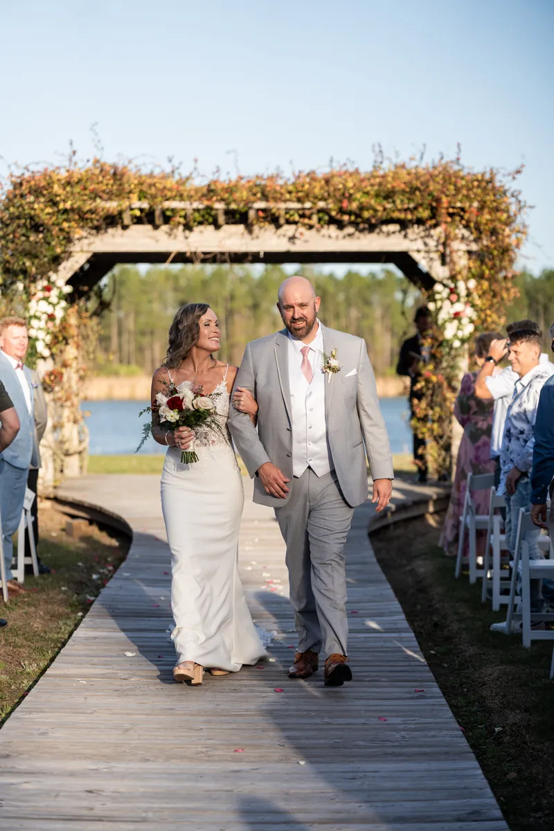 Angela and Bryan exit through a sparkler-lined tunnel while guests celebrate around them at Tringali Barn, with string lights