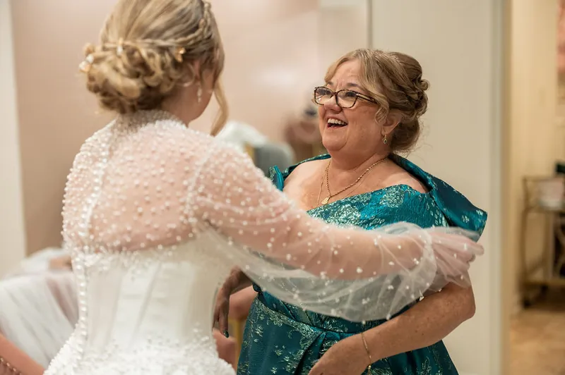 Anna embraces a family member in a teal dress while wearing her beaded wedding cape at The Treasury on the Plaza, St.