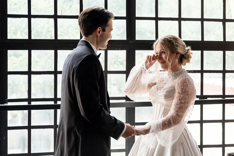 Rafael and Anna hold hands during their ceremony, framed by geometric patterned glass windows.