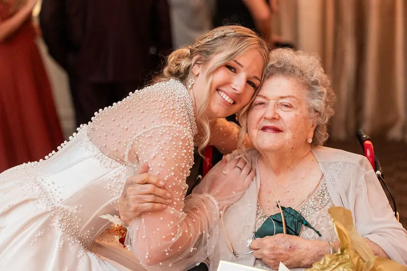 Anna smiles while embracing an older woman in a cream lace dress at The Treasury on the Plaza.