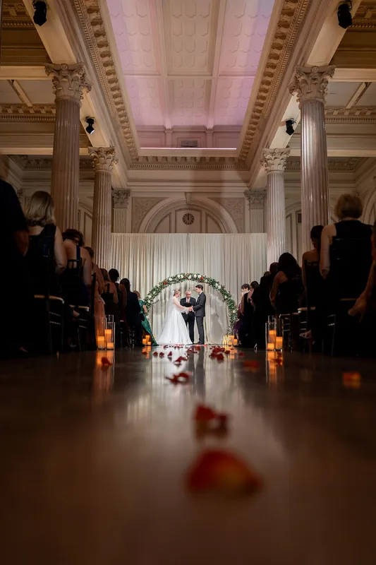 Symmetrical view down the grand hall at The Treasury, lined with candles and red petals, couple visible at far end.