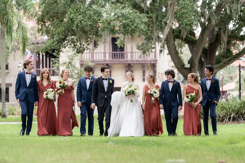 Anna in her white gown stands with groomsmen and bridesmaids across the manicured lawn at The Treasury.