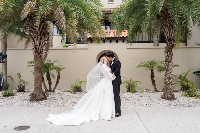 The couple embraces under tall palm trees in the courtyard at The Treasury on the Plaza, Anna's train flowing across