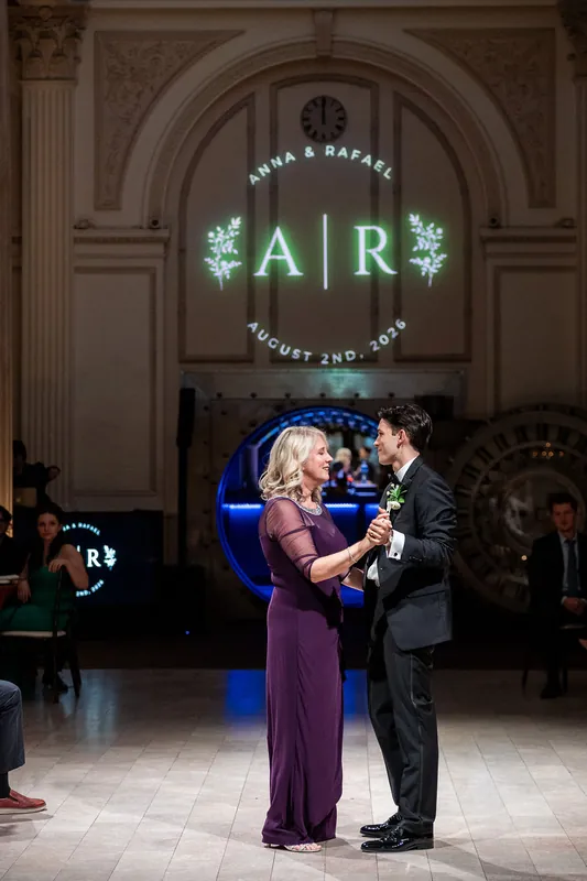 Rafael and Anna stand beneath a neon monogram reading "AR" during their first dance at the venue.