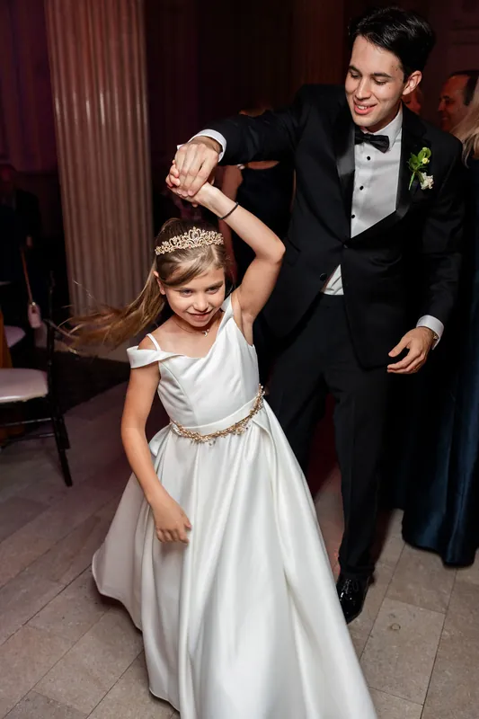 Rafael in a black tuxedo swings a young girl in a white dress across the dance floor at The Treasury on the Plaza, St.