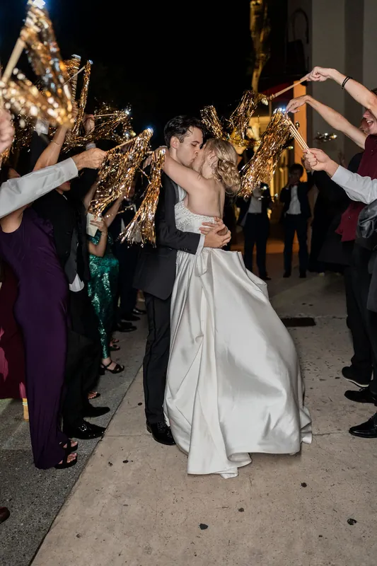 Guests hold golden palm fronds overhead as Anna twirls beneath them in her white gown outside The Treasury on the Plaza, St.