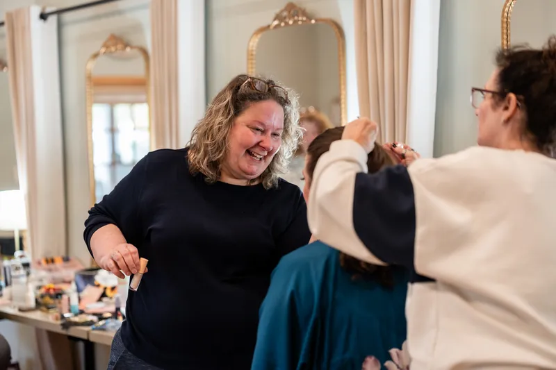 Makeup artist laughing while working on the bride's hair in the getting-ready suite at Fountain of Youth