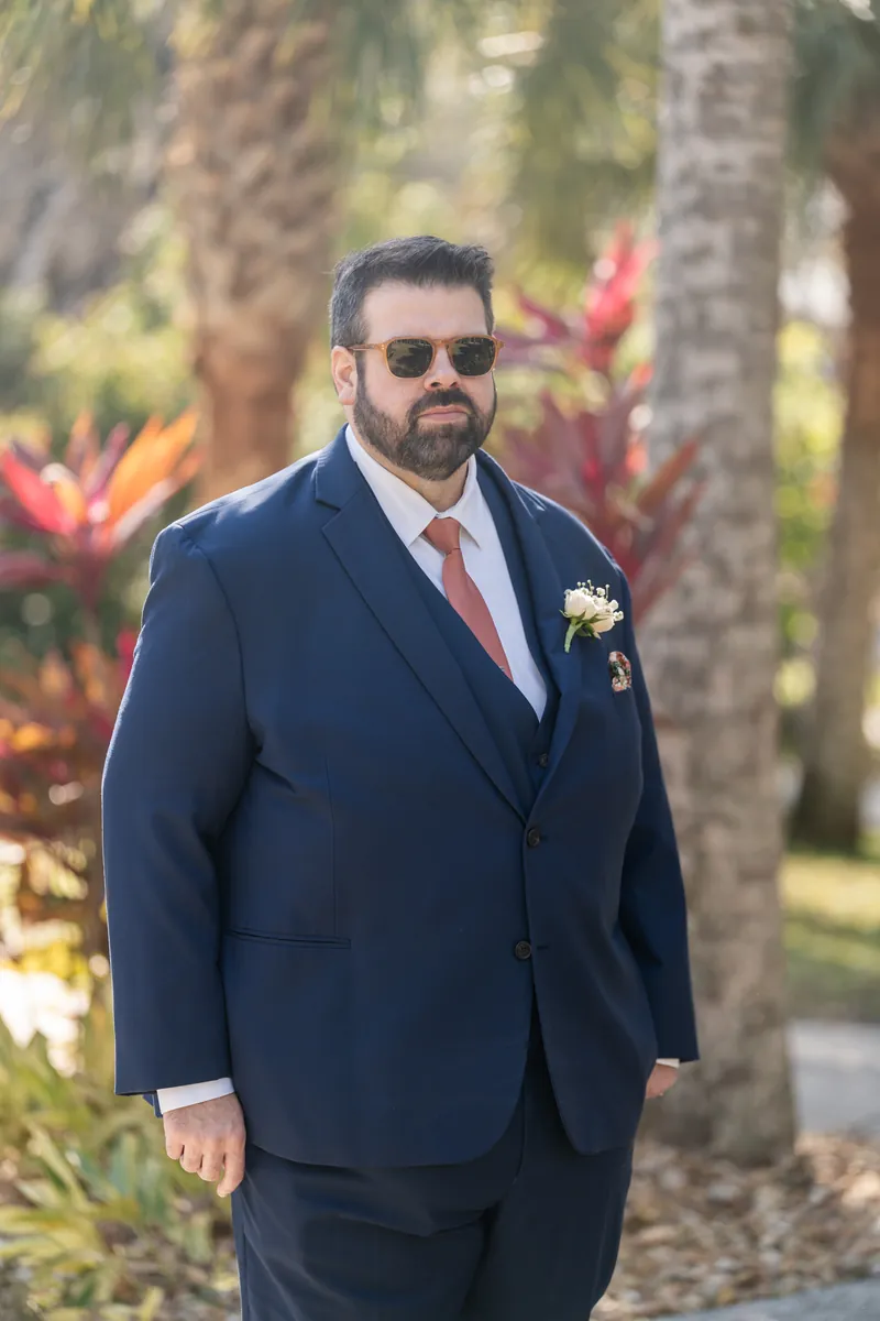 The groom in sunglasses standing among tropical plants and palm trees in the Fountain of Youth gardens