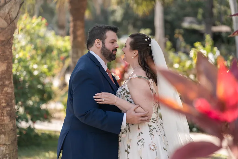 The couple embracing during their first look with red tropical foliage in the foreground