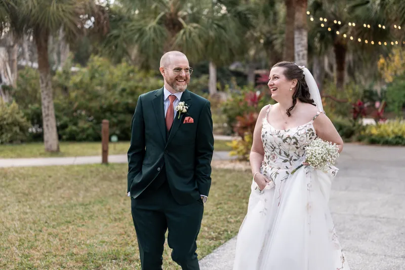The bride and the best man walking and laughing together along a path at Fountain of Youth with string lights in the background