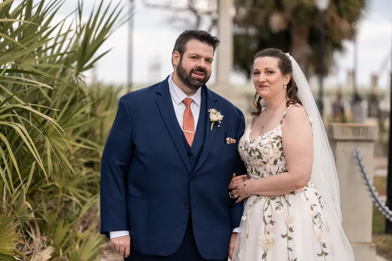 Anne and Chase standing together near the bayfront with palm fronds framing the portrait